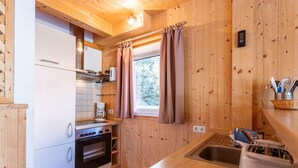 A compact kitchen with wooden walls, a built-in oven, a coffee maker, and a window with curtains. - Appealing Chalet With Terrace (Stadl-Predlitz)