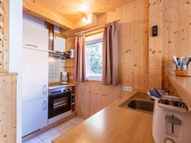 Cocina compacta con paredes de madera, horno empotrado, cafetera y ventana con cortinas.