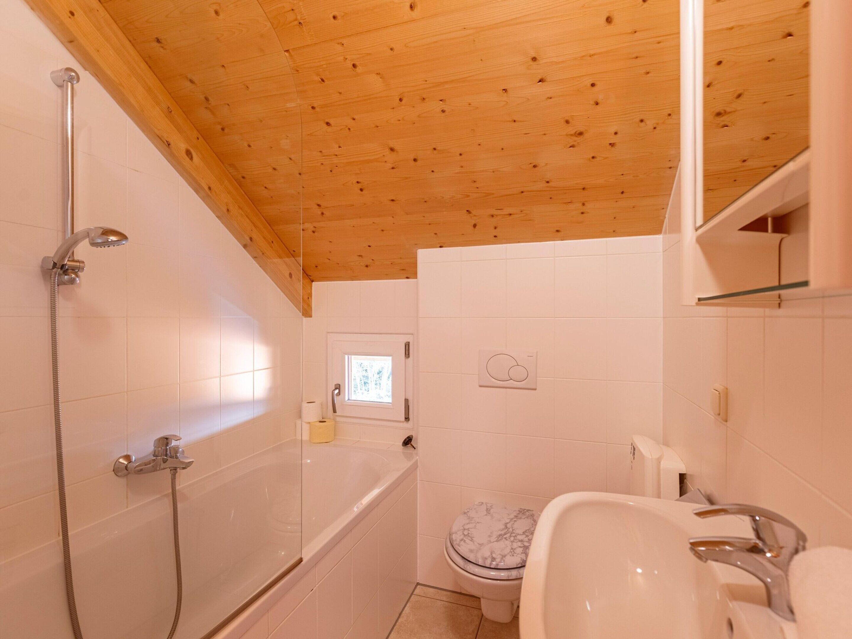 Un baño con techo de madera, una bañera, un inodoro y un lavamanos.