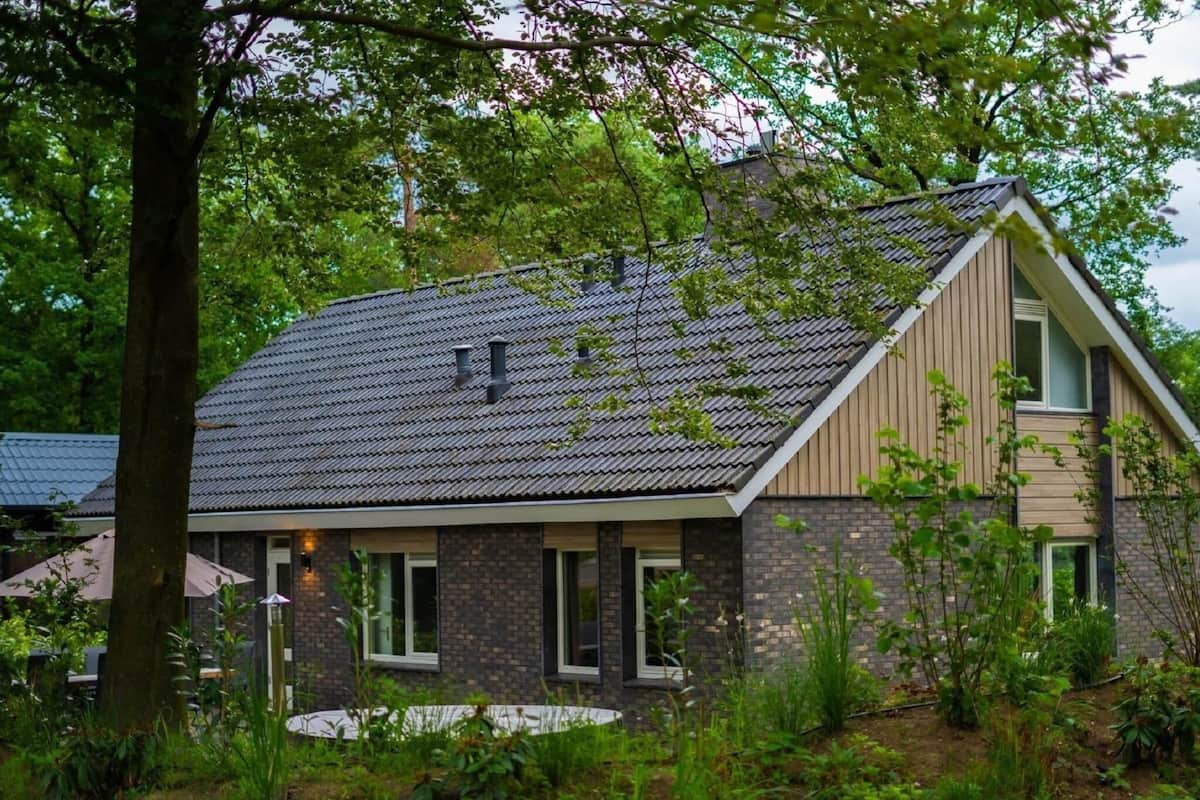 A modern house with a sloped roof, brick exterior, and a large garden area.