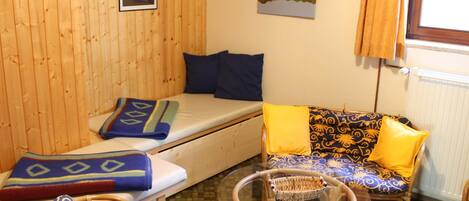 A cozy room with a wooden wall, a sofa with patterned cushions, a small table with a basket, and a window with curtains.