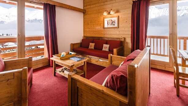Eine Holzhütte mit rotem Teppich, Holzmöbeln, einer Couch, einem Tisch und einem Bild an der Wand.