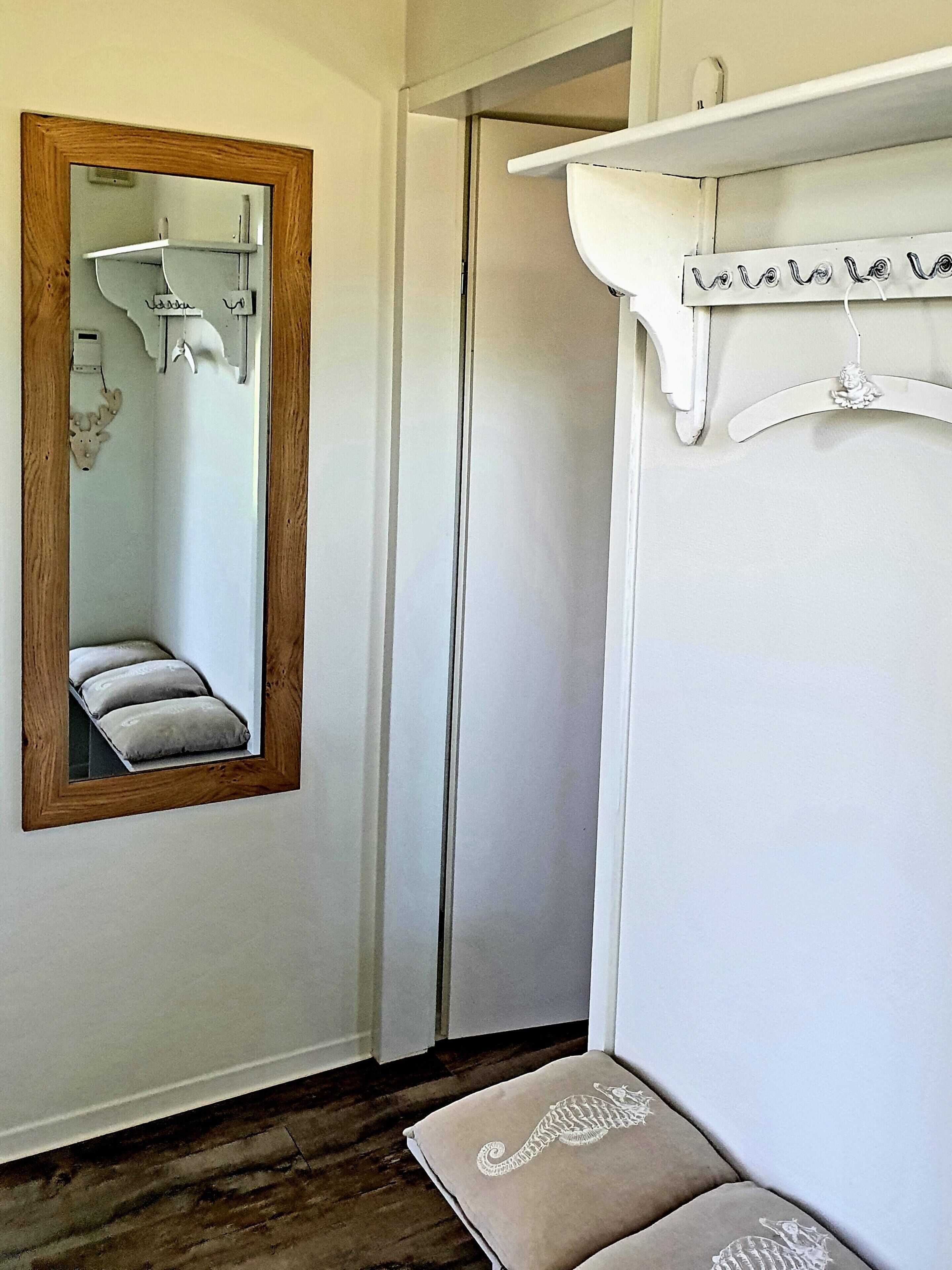 Une chambre à coucher avec un miroir à cadre en bois, une armoire blanche, un lit avec une tête de lit et une table de chevet avec une lampe.