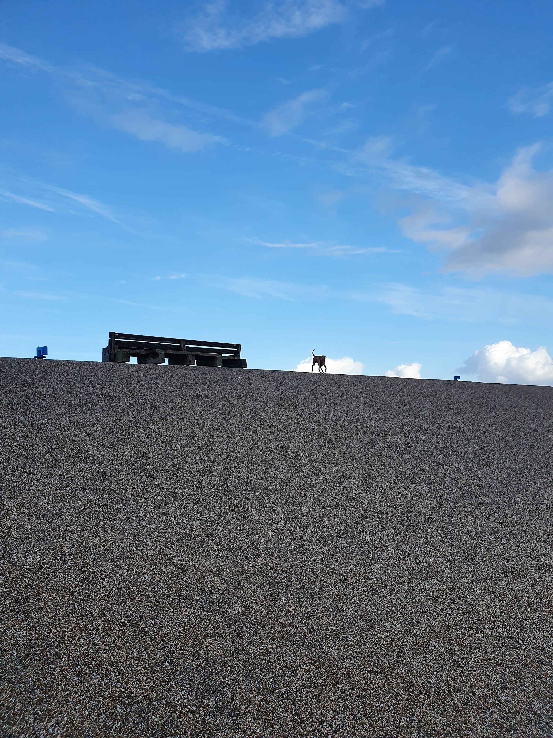 A large, open outdoor area with a flat, textured surface, possibly a plaza or courtyard, under a clear blue sky with scattered clouds.