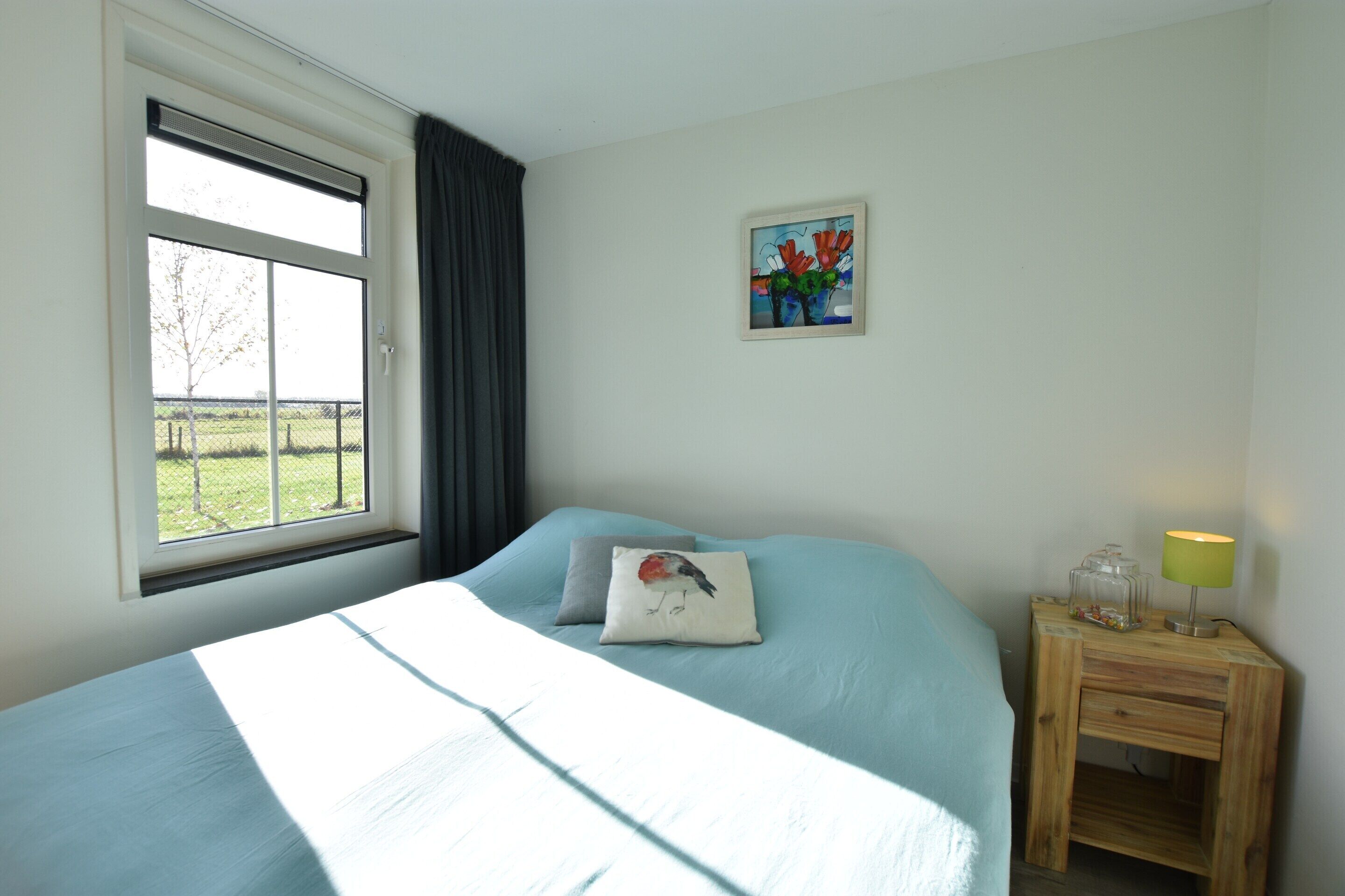 A bedroom with a bed, a window, a nightstand, and a painting on the wall.