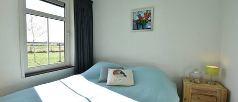 A bedroom with a bed, a window, a nightstand, and a painting on the wall.