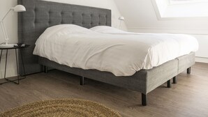 A modern bedroom with a grey upholstered bed, white bedding, and a small bedside table with a lamp. - Farmhouse in De Cocksdorp Near the Beach (De Cocksdorp)