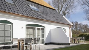 A modern house with a sloped roof, large windows, and a patio area with outdoor furniture. - Farmhouse in De Cocksdorp Near the Beach (De Cocksdorp)