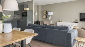 A modern living room with a grey sofa, wooden dining table, and a kitchen in the background. - Farmhouse in De Cocksdorp Near the Beach (De Cocksdorp)