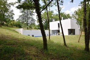 A modern house with a flat roof, large windows, and a grassy yard with trees. - Holiday Home in Boissieres With Private Pool (Boissieres)
