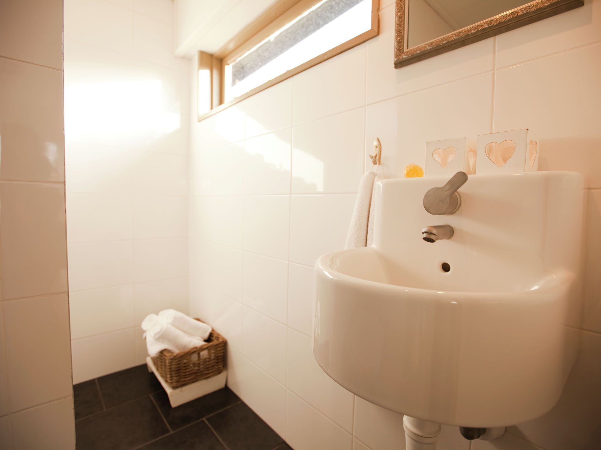 Une salle de bain avec un lavabo blanc, un petit panier contenant des serviettes et un miroir au mur.