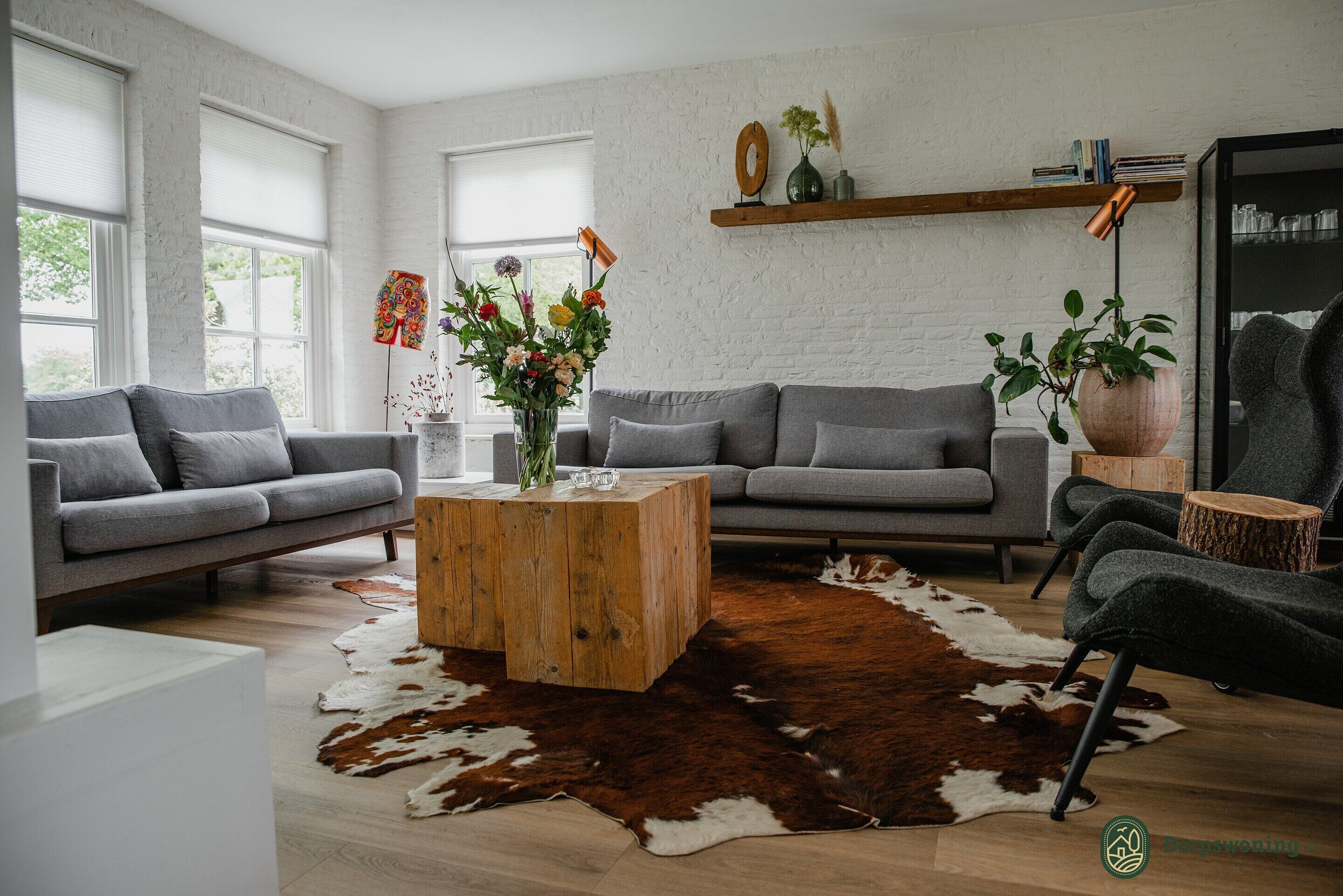 Een moderne woonkamer met twee grijze banken, een houten salontafel en een kleden van koeienhuid.