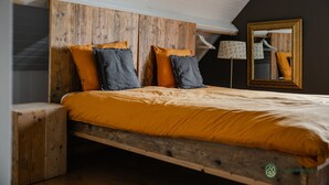 A bedroom with a wooden headboard, a bed with orange bedding, and a mirror on the wall. - Forest Cottage Near Leenderbos (Leende)