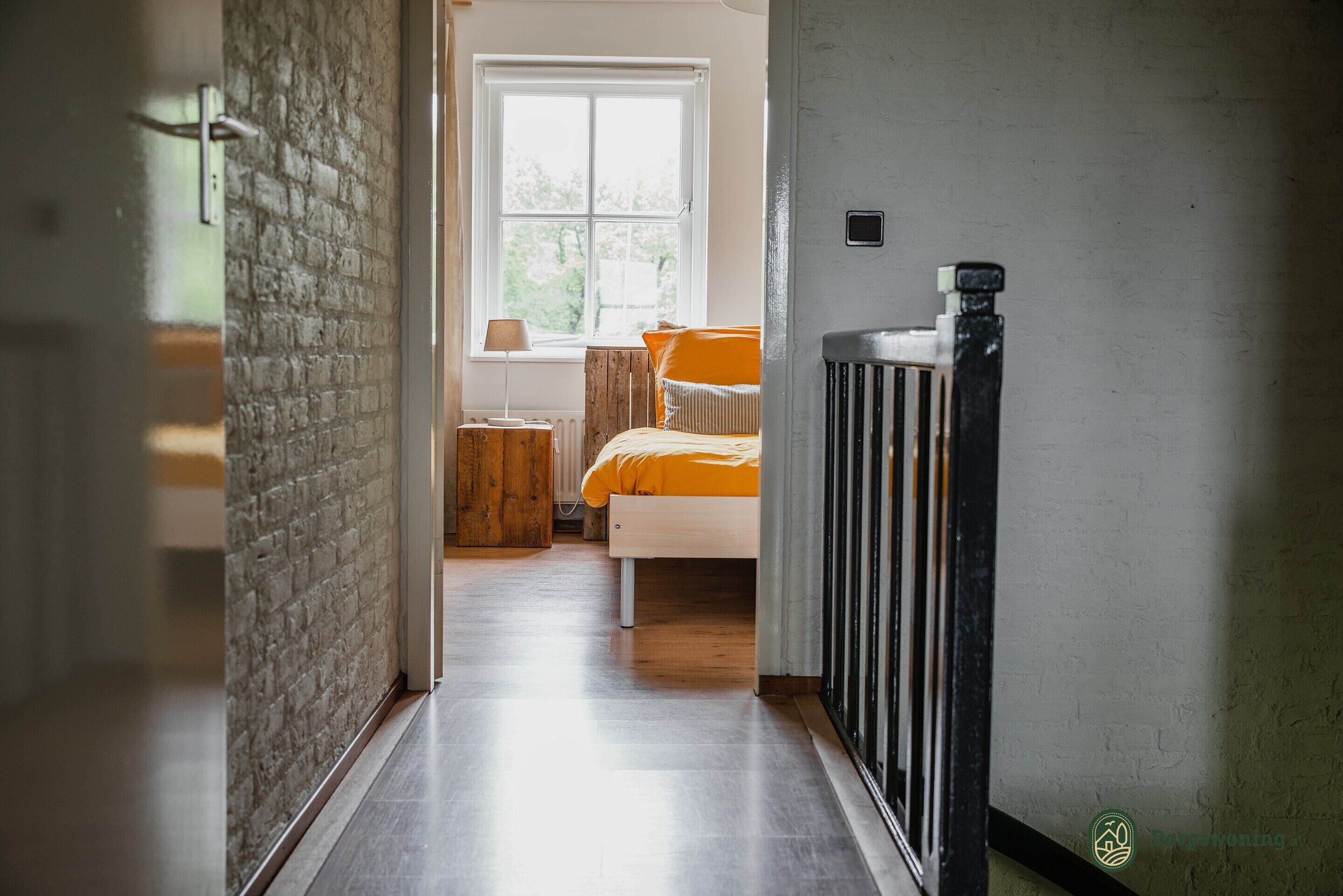 A hallway leading to a bedroom with a bed, a nightstand, and a window.