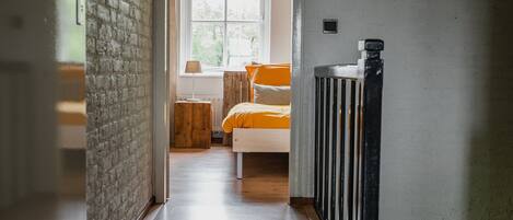 A hallway leading to a bedroom with a bed, a nightstand, and a window.