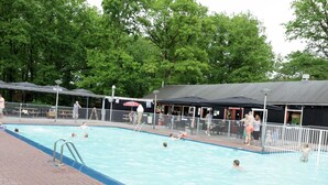 A swimming pool with a fenced area, surrounded by trees and covered structures. - Glamping With Comfort in Ijhorst (IJhorst)