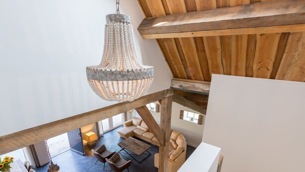 Une pièce aux hauts plafonds, avec des poutres apparentes, un grand lustre et un coin salon confortable comprenant un canapé et des fauteuils.