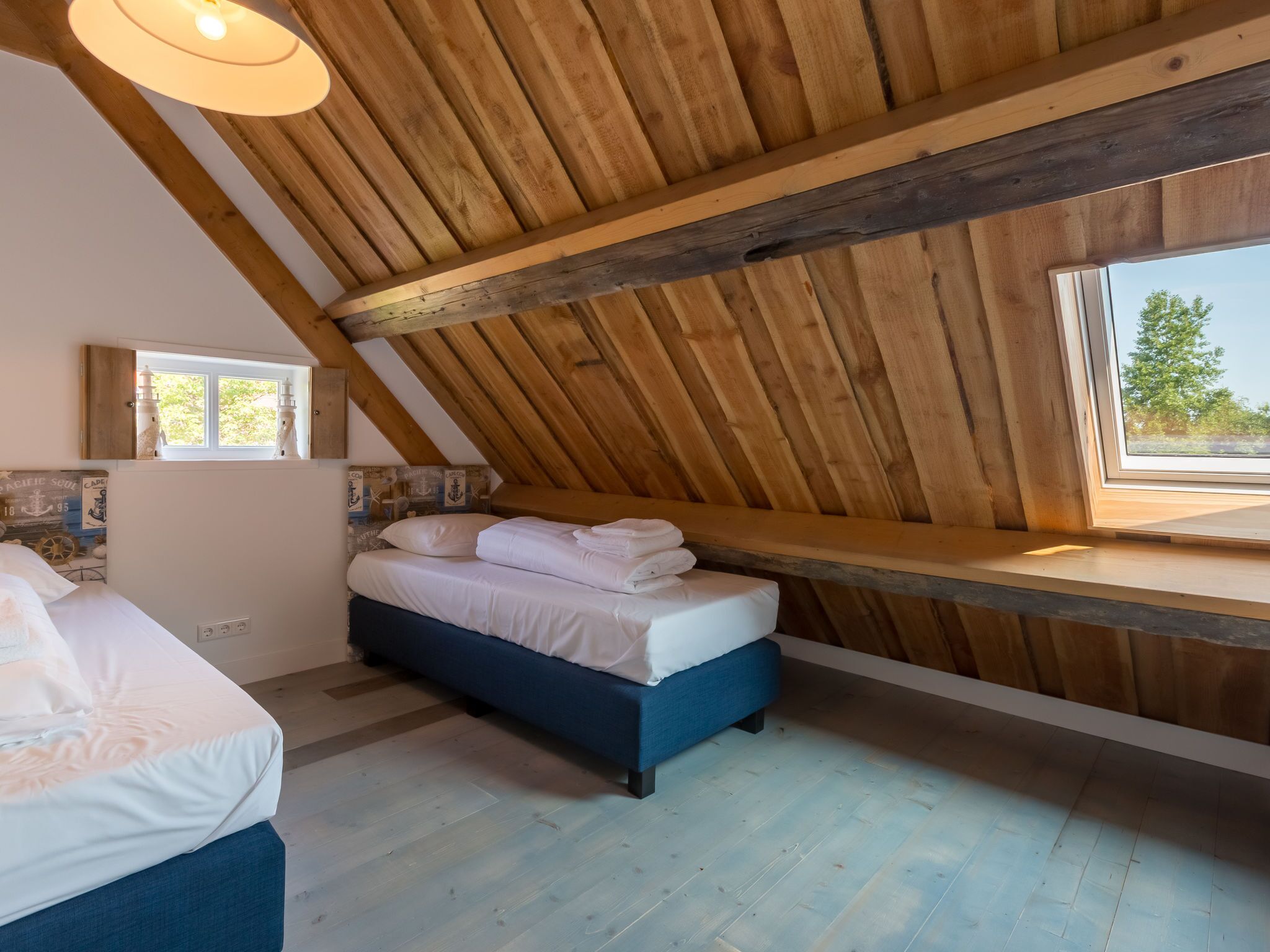 Un dormitorio con techo inclinado, una cama, un banco y una ventana con vistas a árboles.