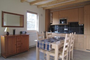 Una cocina con armarios de madera, microondas y una mesa de comedor con sillas.