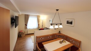 Un coin repas avec une table et des bancs en bois, un téléviseur fixé au mur et une lampe.