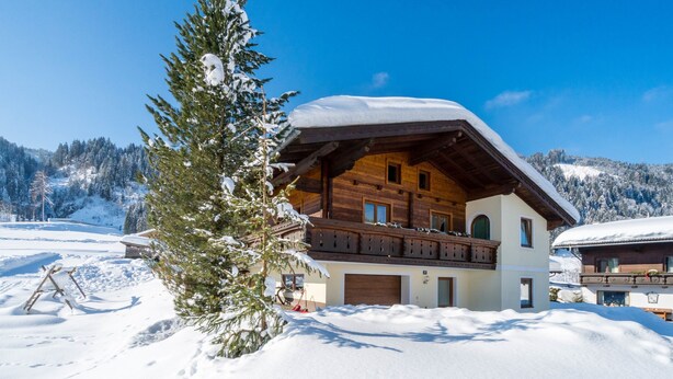 Un chalet en bois doté d’un balcon, entouré de montagnes enneigées.