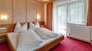 A wooden-paneled bedroom with a large bed, two bedside tables, a radiator, and a window with sheer curtains.