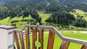 A wooden balcony railing overlooking a mountainous landscape with dense forests and a clear sky.