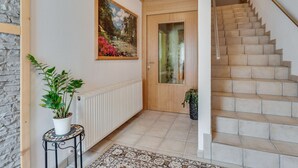 A staircase with beige tiles, a wooden door with a glass panel, and a painting of a landscape on the wall.