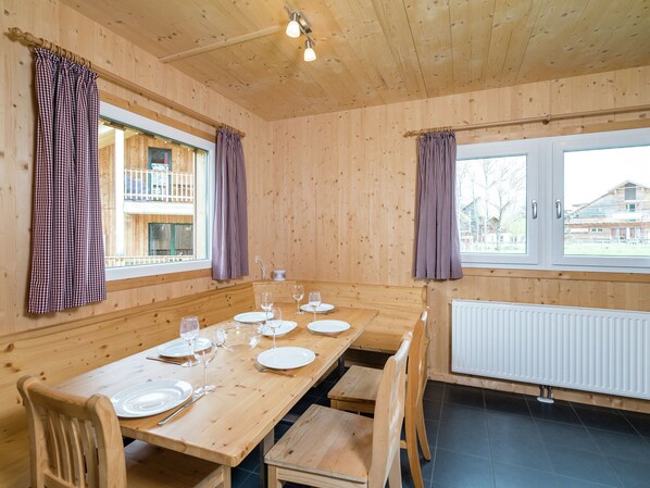 Ein Esszimmer mit Holzboden, einem Tisch für vier Personen, zwei Fenstern mit Vorhängen und Blick auf ein Gebäude.