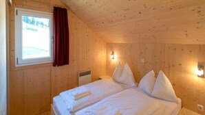 A wooden cabin bedroom with a bed, two bedside tables, a window with curtains, and a wall-mounted light fixture. - Chalet With Whirlpool tub (Sankt Georgen am Kreischberg)