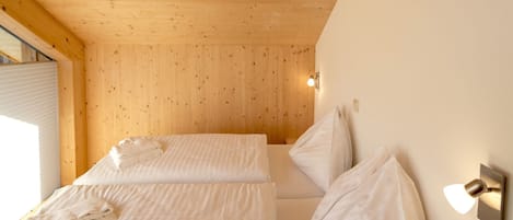 Une chambre avec deux lits, un plafond en bois et un luminaire fixé au mur.