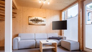 Un soggiorno moderno con una parete in legno, un divano grigio, un tavolino in legno e una televisione a schermo piatto fissata alla parete.