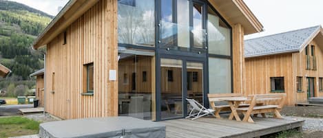 Una cabaña de madera con un gran ventanal, mobiliario exterior y un jacuzzi.