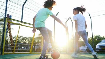 Two people playing soccer on a green field with a goalpost and a fence in the background.