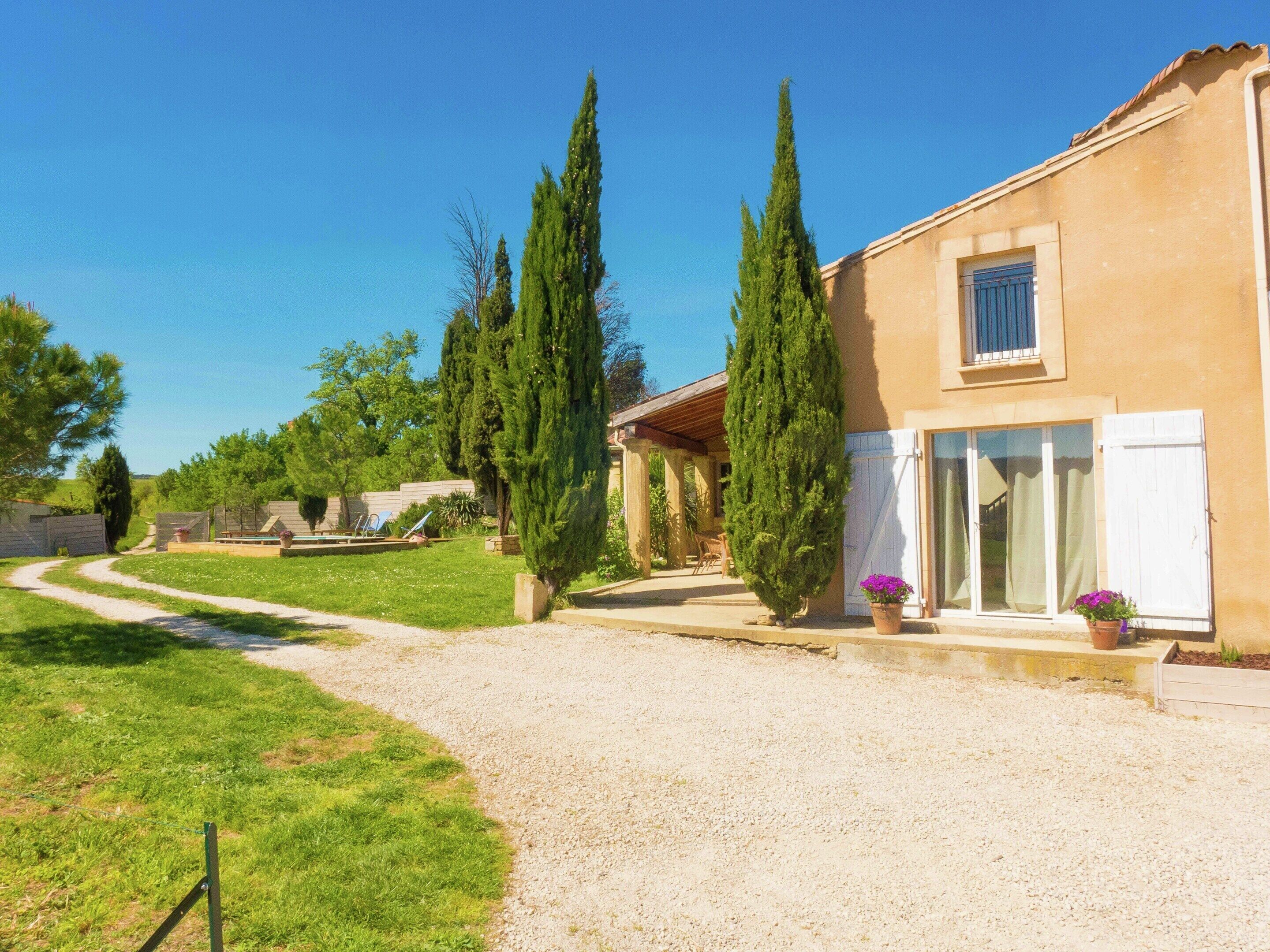 Uma casa com entrada por caminho de pedras, varanda coberta e jardim com ciprestes.