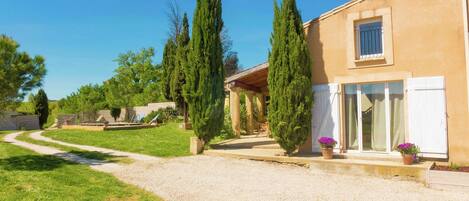 Uma casa com entrada por caminho de pedras, varanda coberta e jardim com ciprestes.