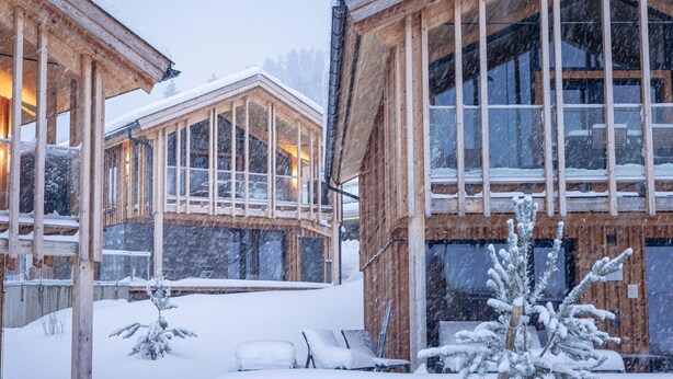 Una cabaña de madera con ventanas grandes y fachada cubierta de nieve.