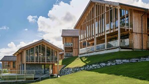 Un edificio moderno de madera con amplios ventanales y balcones, ubicado en una colina cubierta de césped.