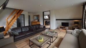 A modern living room with a brown leather sofa, a beige sofa, and two coffee tables with decorative items. A wooden staircase is visible in the background. - Unique Holiday Home in Stramproy near Forest (Stramproy)