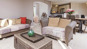 A living room with two sofas, a coffee table, wicker furniture, and a kitchen in the background. - Villa in Cazals With Pool & Lake Nearby (Cazals)
