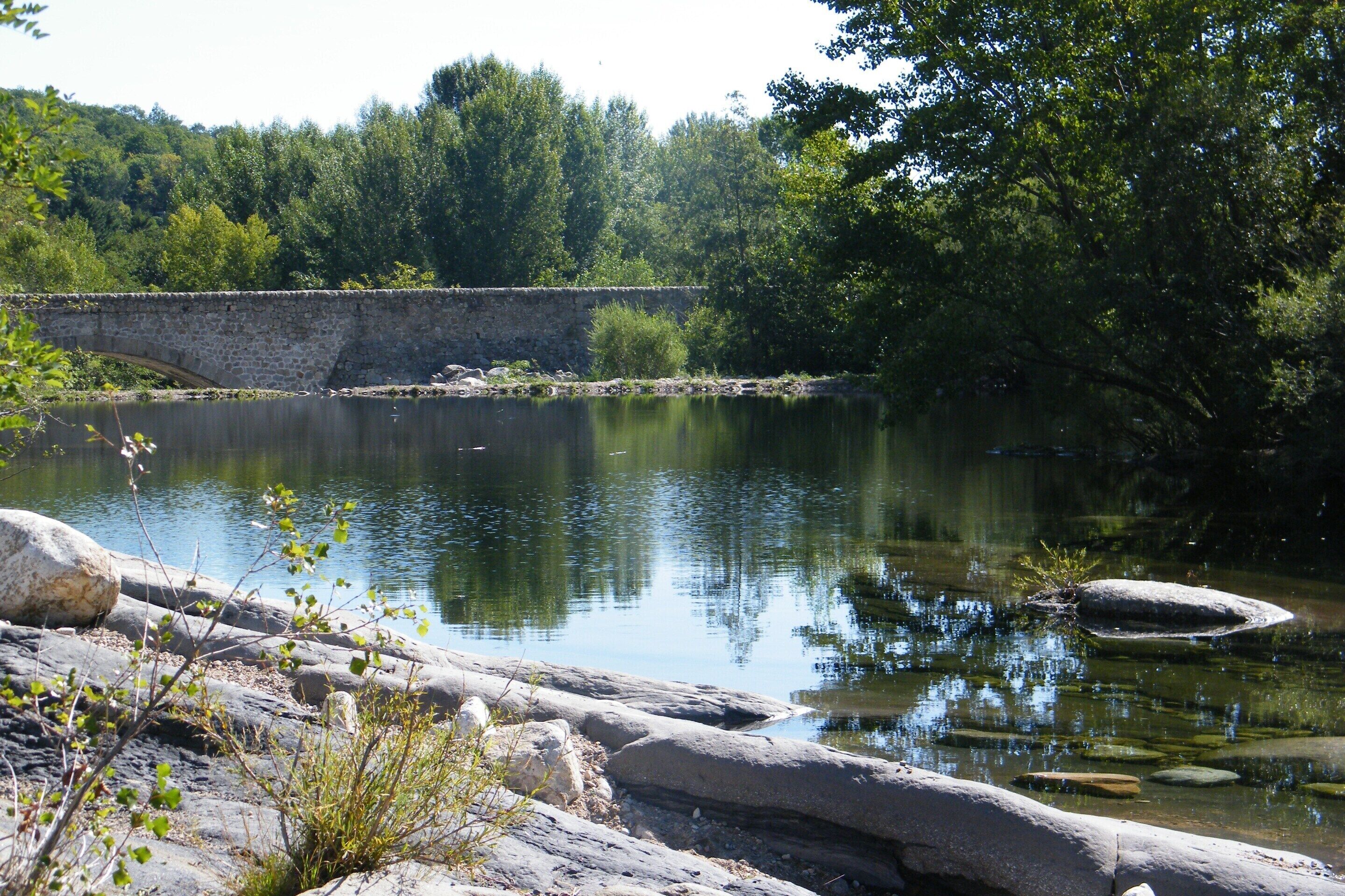 Un puente de piedra sobre un río tranquilo, rodeado de árboles y rocas.