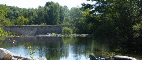 Un puente de piedra sobre un río tranquilo, rodeado de árboles y rocas.