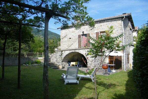 Ein Steinhaus mit Balkon, Grill und überdachter Außenbereich zum Sitzen.