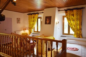 A room with a wooden staircase, two beds with yellow curtains, a window with a view, and a radiator.