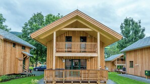 A two-story wooden cabin with a balcony, surrounded by a well-maintained lawn and trees. - Spacious Chalet With Infrared Sauna (Sankt Georgen am Kreischberg)