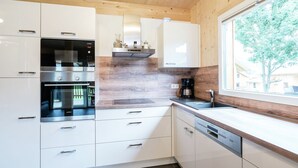 A modern kitchen with white cabinets, stainless steel appliances, and a wooden ceiling. - Spacious Chalet With Infrared Sauna (Sankt Georgen am Kreischberg)