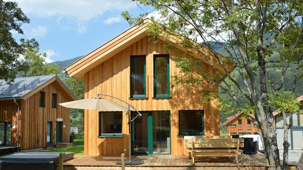 Een houten chalet met terras, jacuzzi en een bank.
