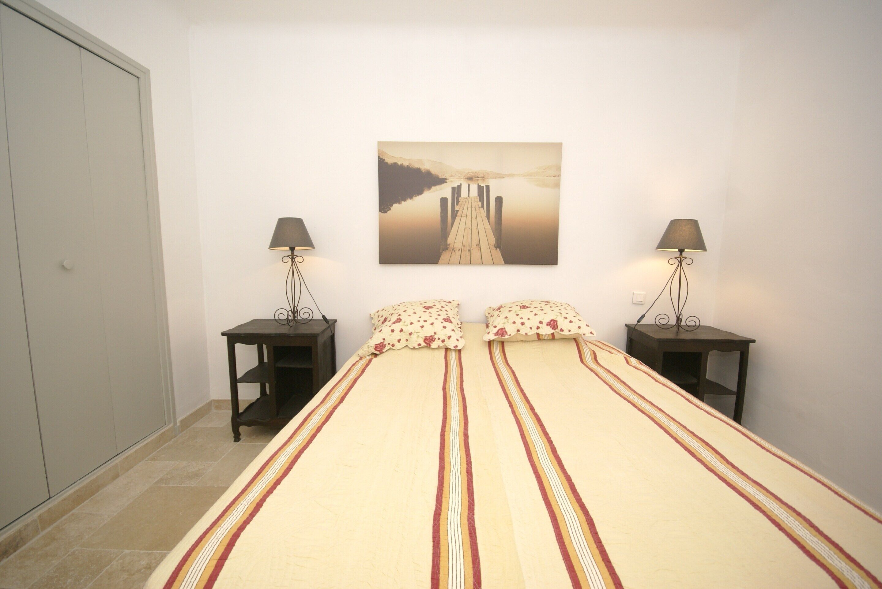 A bedroom with a bed, two bedside tables, a wall-mounted lamp, and a framed picture.