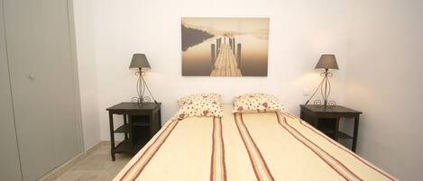 A bedroom with a bed, two bedside tables, a wall-mounted lamp, and a framed picture.