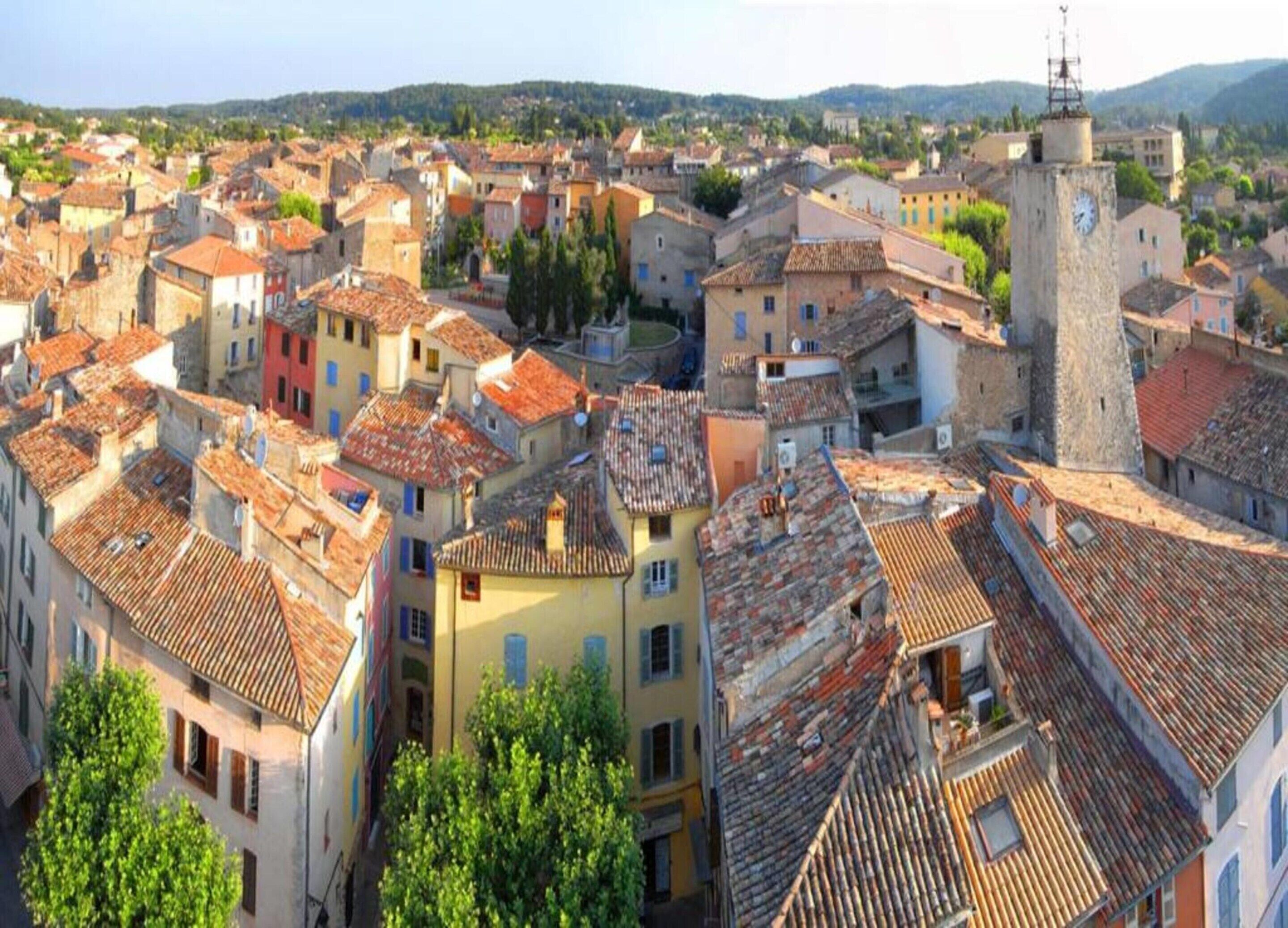 Un área urbana densamente poblada con edificios históricos, una destacada torre del reloj y un paisaje montañoso de fondo.